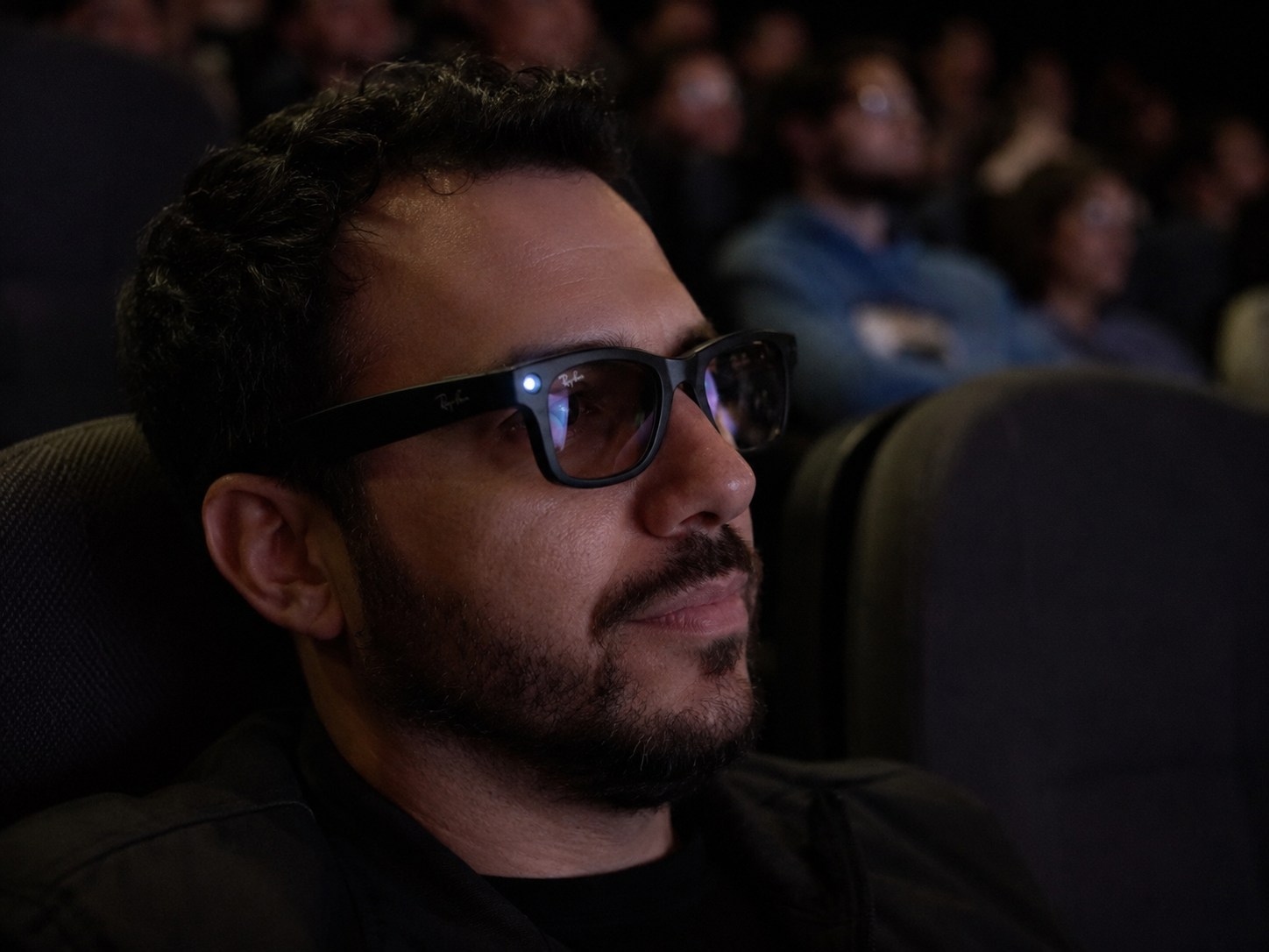 A man wearing Ray-Ban Meta glasses with the white capture light illuminated in a cinema