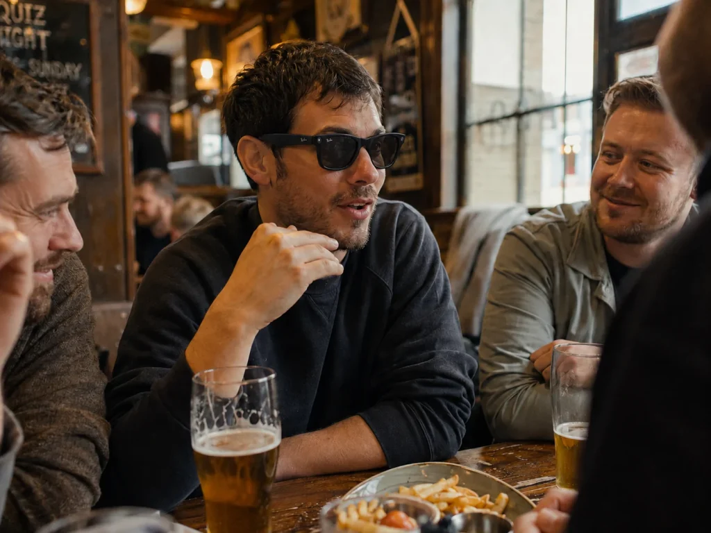 Friends talking in a pub while one man wears AI glasses with the white recording light visible